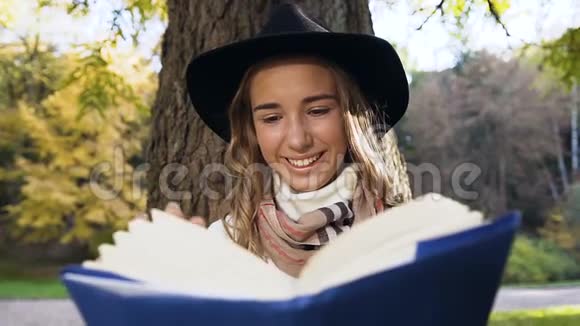 微笑的金发女人戴着时尚的帽子和围巾在城市公园看书视频的预览图