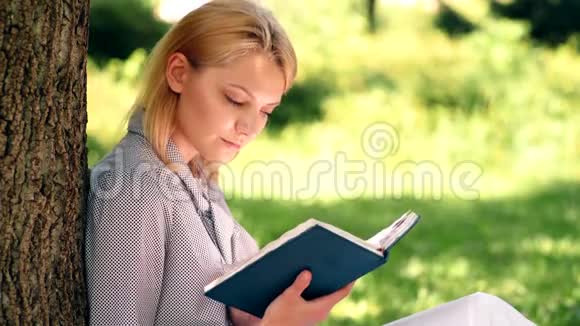 那个女孩从坐在公园草地上的笔记本上看书女学生准备在公园上课这就是视频的预览图