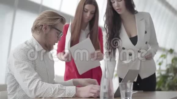 肖像紧张的男人坐在现代办公室桌前拿着上网本收集两个女同事的文件视频的预览图