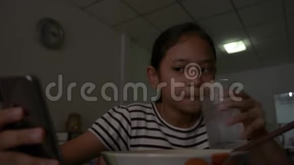 可爱的亚洲女孩一边吃炸面一边从智能手机看在线视频视频的预览图