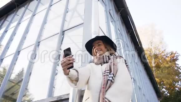 戴着帽子的漂亮女孩在公园里的智能手机上占有一席之地视频的预览图