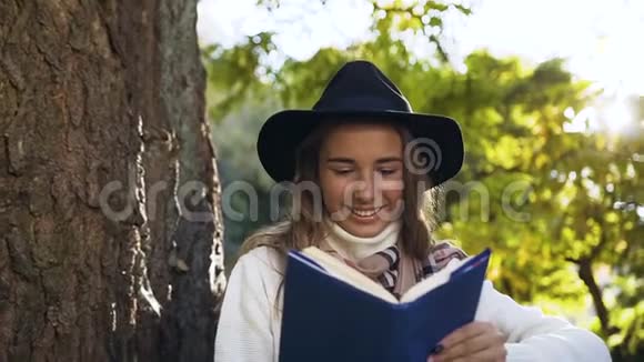 戴着黑帽子的漂亮年轻女人在绿色公园背景上看书视频的预览图