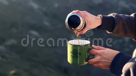 一个女孩的特写镜头她的手把茶从热水瓶里倒进山里的杯子里视频的预览图