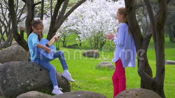 两个小女朋友在城市公园玩牛仔裤吉他和唱歌视频的预览图