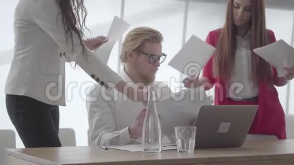肖像紧张的男人坐在现代办公室桌前拿着上网本收集两个女同事的文件视频的预览图