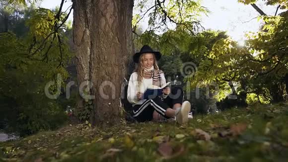可爱的女孩戴着帽子看书坐在公园的草地上视频的预览图