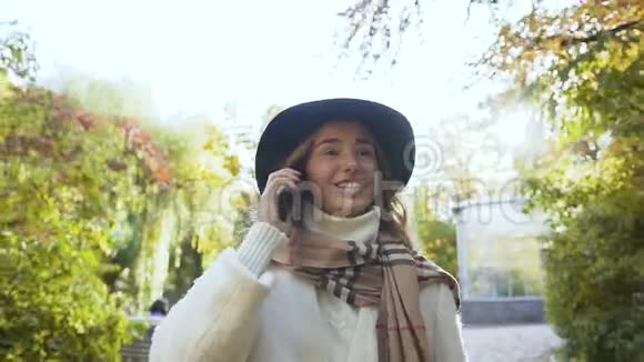 穿着白色外套的时髦女孩在绿色公园里和手机上的人说话视频的预览图