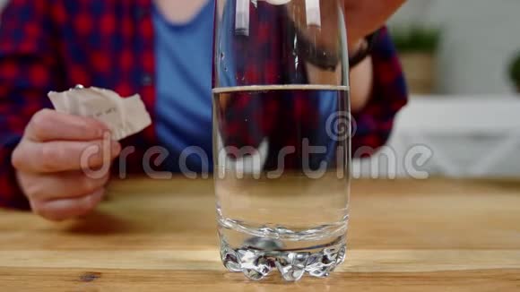 女孩把泡腾的药片扔进桌子上的一杯水里视频的预览图