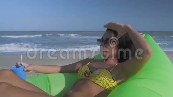 戴着太阳镜的贴身美女躺在一个绿色充气枕头上手里拿着鸡尾酒视频的预览图