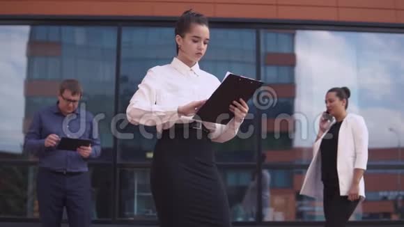 商业女孩正在看工作文件而她背后是一个商人和商业妇女高清高清视频的预览图