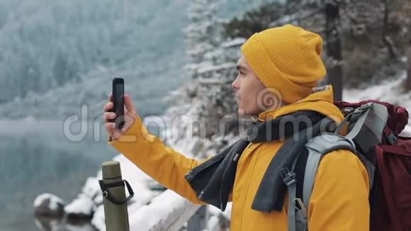 穿着黄色夹克的年轻帅哥站在美丽的山上徒步旅行者拍摄冬季自然的视频这就是视频的预览图