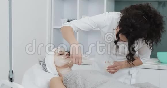 美容师在水疗沙龙给面部病人戴上白色面具身体护理健康生活方式概念视频的预览图