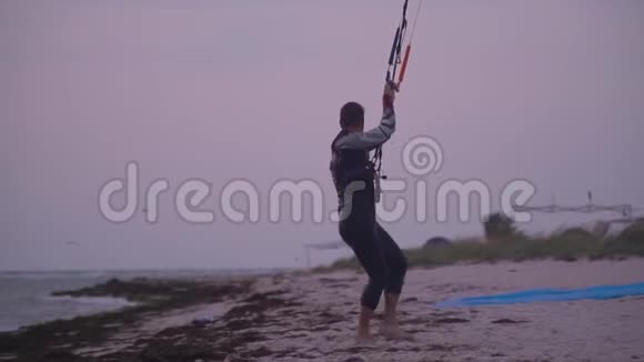 一个穿着湿衣服的人拿着一束训练风筝沿着海滩散步视频的预览图