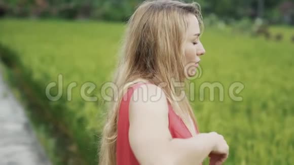 一个年轻的金发女郎站在稻田里把脸转到镜头里用手开始表演舞蹈视频的预览图