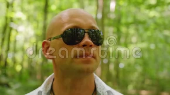一个戴太阳镜的秃头在树林里唱歌和散步的肖像绿树夏天森林大自然关门视频的预览图