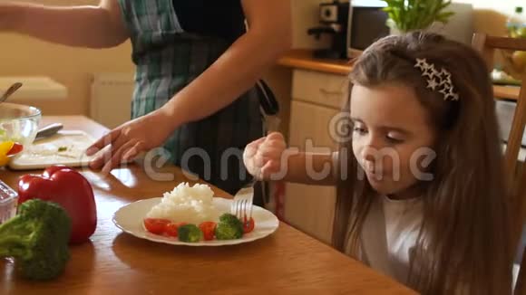 女孩正在厨房里吃早餐在她妈妈旁边切蔬菜适当的婴儿食品视频的预览图