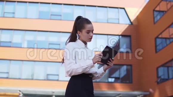 年轻的商业女孩站在商业大厦附近手里拿着一块平板电脑高清高清视频的预览图