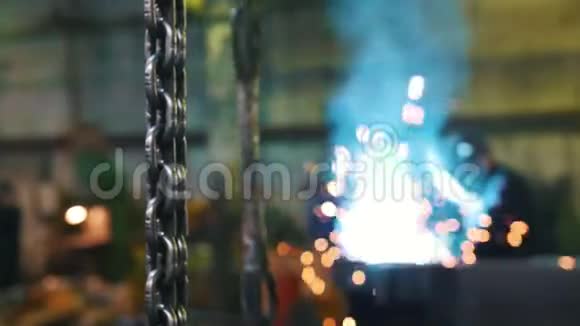 建筑工厂挂在前景上的金属链一个男人在背景上焊接蓝色火花和光视频的预览图