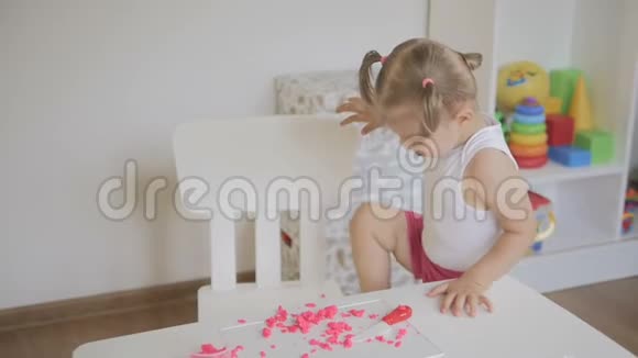 一个小女孩坐在一间明亮的房间里的一张白色桌子后面雕刻着一个粉红色的视频的预览图
