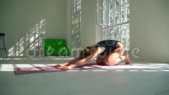 年轻的红发技能健康的白种人女人在白色的大房间里的垫子上练习瑜伽年轻女子视频的预览图