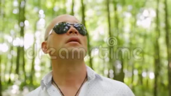 一个戴太阳镜的秃头在树林里唱歌和散步的肖像绿树夏天森林大自然关门视频的预览图