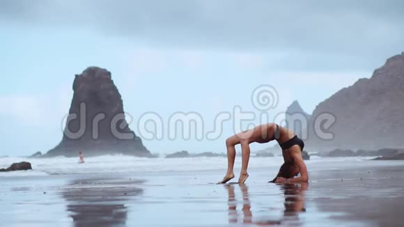 海滩上的女体操运动员做了一个轮子变成了一个姿势桥站在他的手上脚在后面弯曲视频的预览图