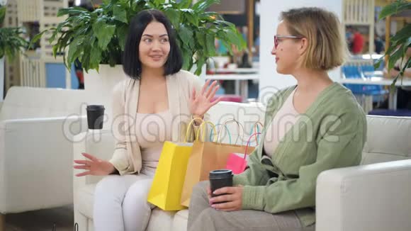 女人从购物袋里拿出一件上衣给朋友看两个女人在笑朋友在享受买衣服视频的预览图