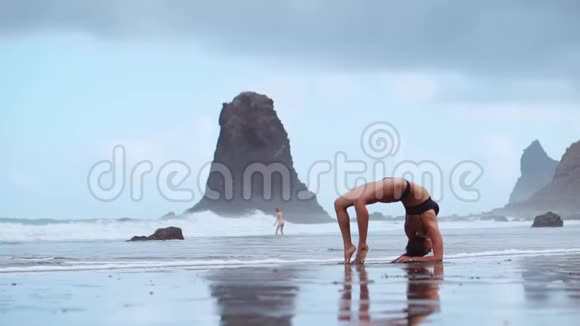 海滩上的女体操运动员做了一个轮子变成了一个姿势桥站在他的手上脚在后面弯曲视频的预览图