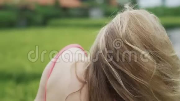 一个年轻漂亮的女孩卷起她的头发把头往后一甩享受阳光和阳光的照射视频的预览图