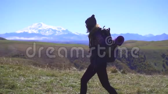 旅游女孩背着背包在群山的背景下散步慢潮侧视视频的预览图