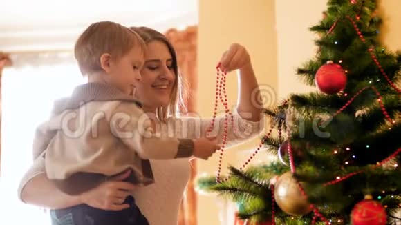 4k镜头可爱的幼儿男孩与母亲装饰圣诞树与彩色花环和珠子视频的预览图