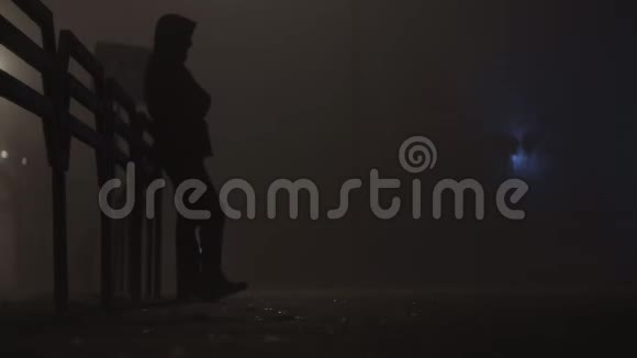 穿着夹克的人站在街上在雾或雾中缓慢地等待夜晚视频的预览图