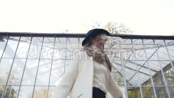 时髦的微笑女人穿着白色外套在公园里转悠看着相机视频的预览图