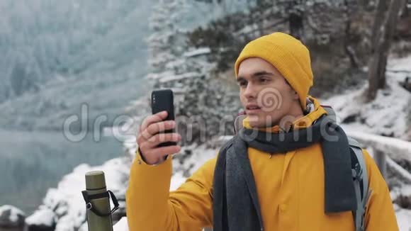 穿着黄色夹克的年轻帅哥站在美丽的山上徒步旅行者拍摄冬天的自然这就是视频的预览图