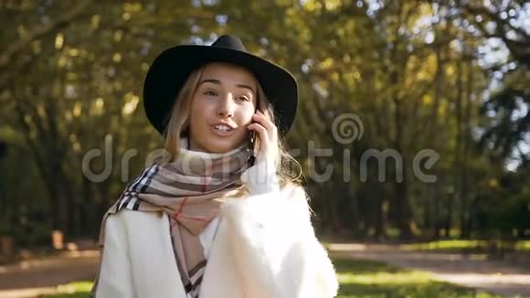 快乐时尚的女孩在秋天公园散步时用她的智能手机和别人交谈视频的预览图