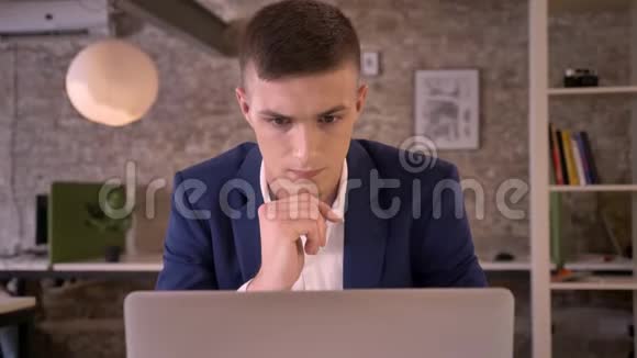 年轻专注的商人在办公室里看着笔记本电脑因为成绩好而高兴手握拳头是的视频的预览图
