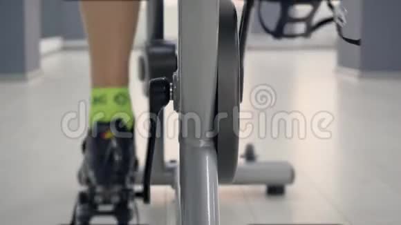 在健身房的自行车课上在静态自行车上关闭腿旋转踏板后视视频的预览图