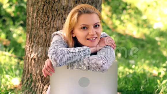女孩坐在公园的草地上靠在笔记本电脑上微笑梦幻般的女孩坐在草地上的公园里视频的预览图