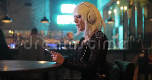 不寻常的女孩戴着白色假发在酒吧里用耳机听音乐视频的预览图