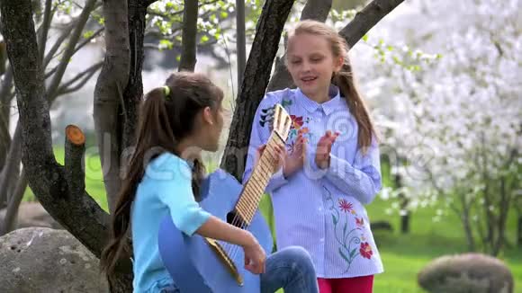 少年女孩弹牛仔裤吉他在春天的公园里唱歌视频的预览图