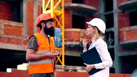 戴着头盔和防护背心的长胡子男人与戴着头盔的女人沟通手里拿着一个文件夹视频的预览图