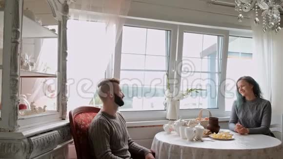 一对年轻漂亮的夫妇穿着温暖的毛衣坐在白色的桌子旁背景是视频的预览图