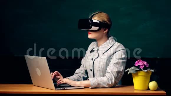 一个女人在笔记本电脑上工作在学生板的背景上戴着虚拟现实的眼镜虚拟的概念视频的预览图