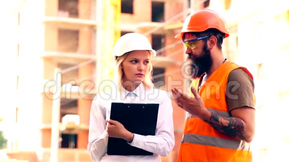 女工程师手里拿着一个文件夹头上戴着一个头盔用一个保护装置与建筑工人沟通视频的预览图
