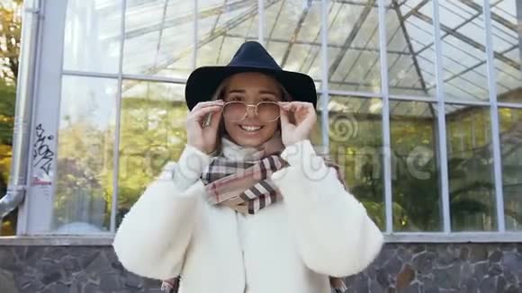 美丽的高加索女人戴着时尚的帽子看着相机戴着太阳镜在公园里近距离射击视频的预览图
