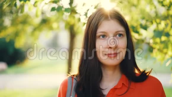 在阳光明媚的夏日迷人的年轻女子站在公园里看着相机和微笑绿色视频的预览图