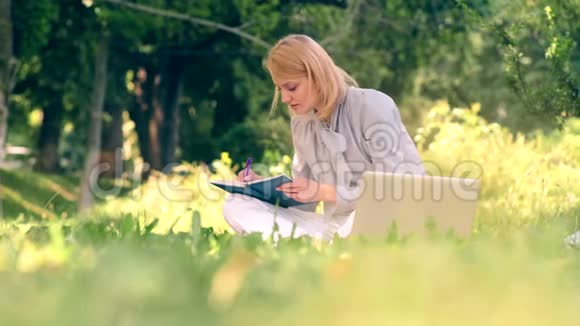 一个女人坐在公园的草地上写着笔记本一个学生坐在公园里准备考试视频的预览图