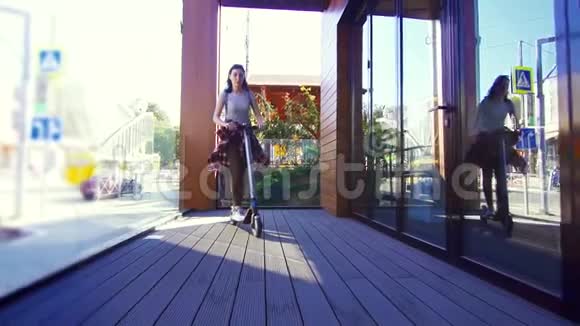女孩骑着电动滑板车在城市的窗户旁边慢悠悠视频的预览图
