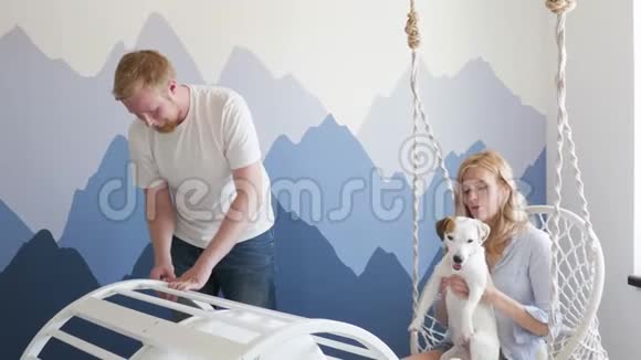 一个男人为一个孩子收集婴儿床他的妻子和一只狗杰克罗素坐在秋千上玩一家年轻的家庭视频的预览图