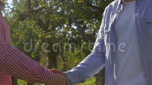 两个面目全非的农民在绿树成荫的土地上握手视频的预览图
